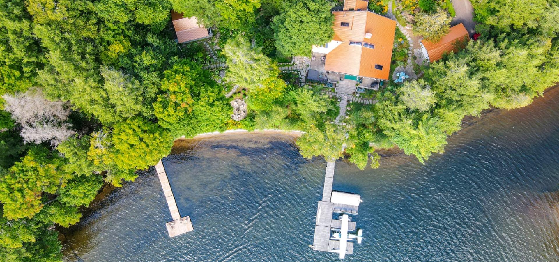 Two cottages surrounded my green trees and with a sandy shore line. Two docks out into the lake. 