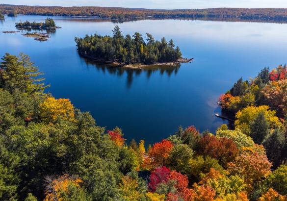 Airborne view of kennisis lake with rich dark blue waters and trees in fall colours. An island is seen in the distance with rock outcroppings.