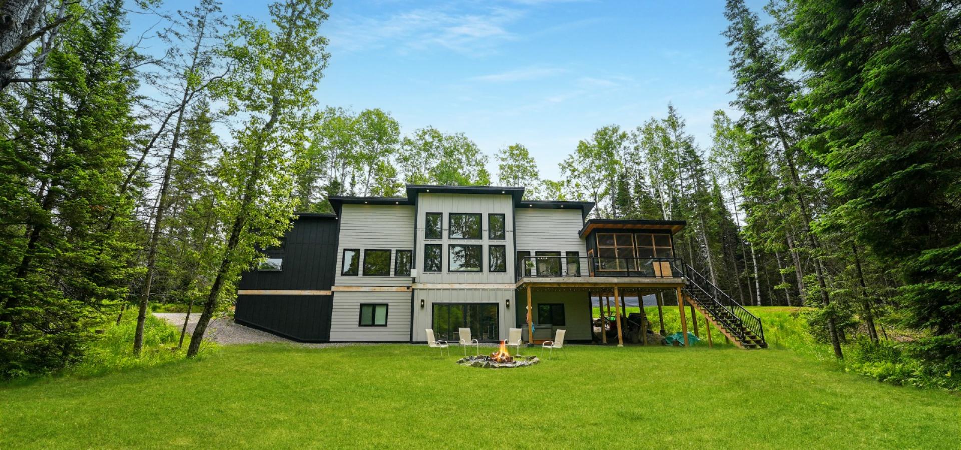 Green grass and trees with leaves, grey and black home, and blue sky.