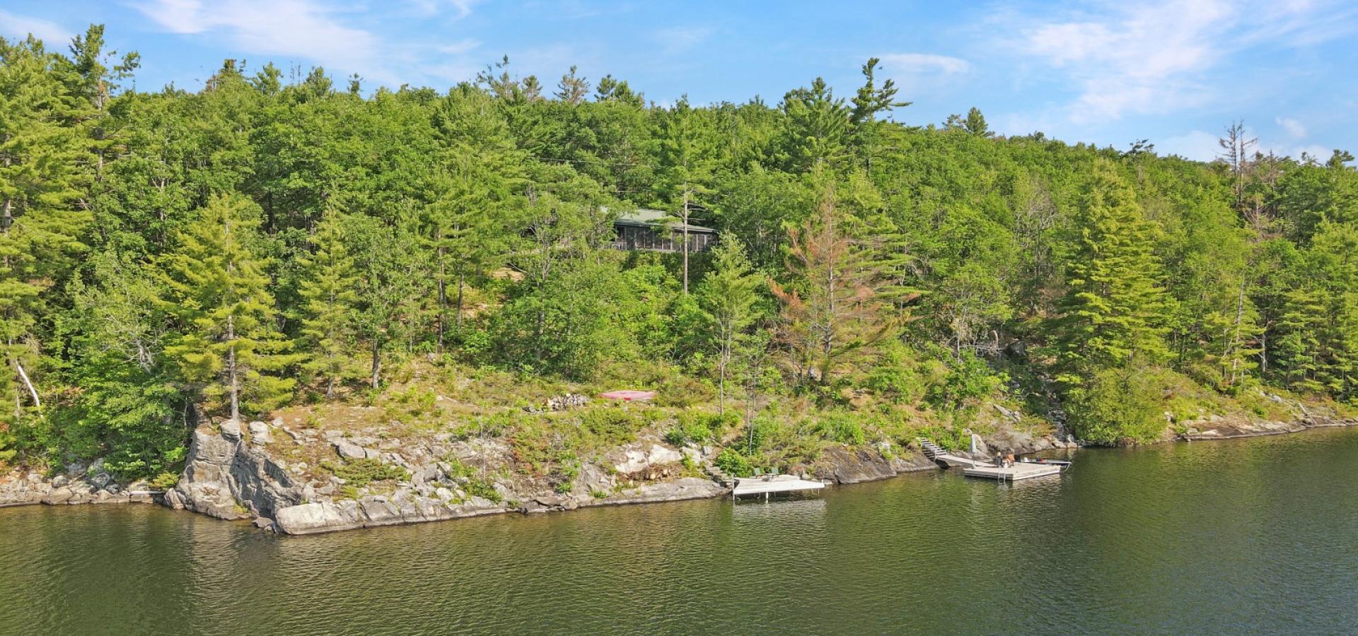 View of a cottage on the hill surrounded by trees and docks out front, with a jump cliff