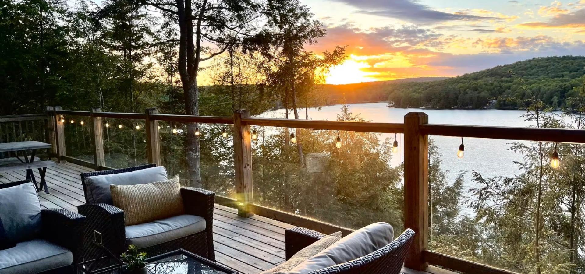 View of the lake with a sunset. Glass railing and 2 chairs, and a couch on the deck.