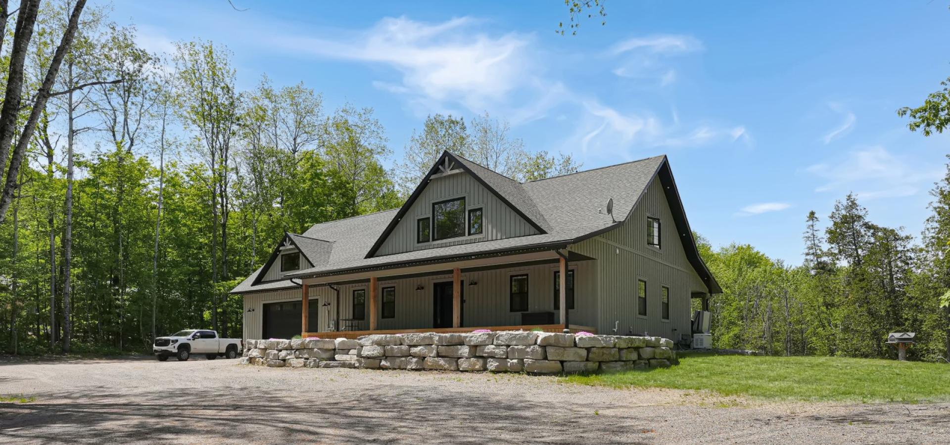 grey house with a covered front porch, stone retaining wall, gravel in front and blue skies