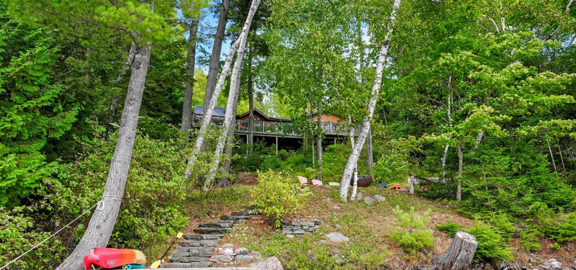 Cottage hidden behind the trees, rocky shoreline, stairs up to firepit area