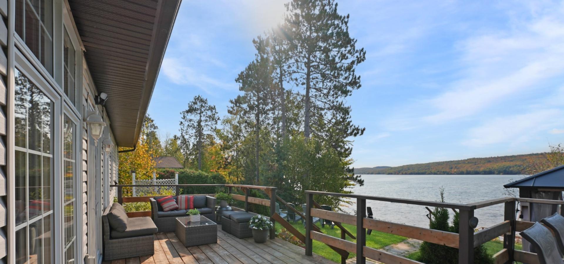 deck with seating area over looking a lake with trees and blue sky