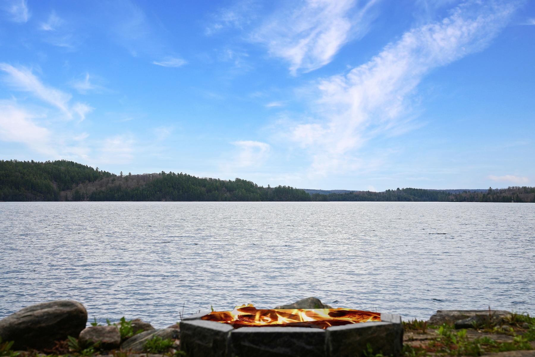 Scenic view of Haliburton Lake looking out over a shoreline firepit on a blue sky sunny day.