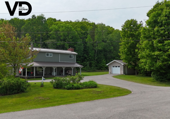 Grey house with full covered porch, detached garage with white door and paved laneway