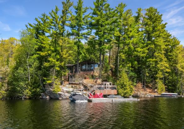 cottage hidden with trees, multi tier decking, red chairs on the dock and blue skies