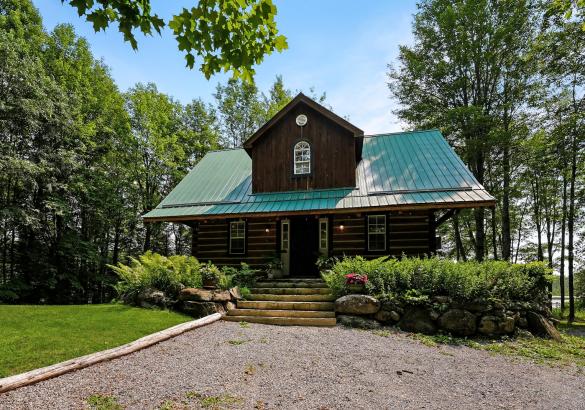 Lot home with green metal roof, stone stairs leading up too, bushes and gravel laneway