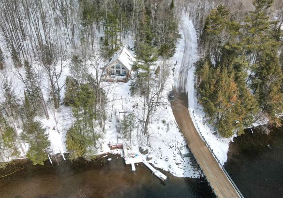 Aerial view of a property with trees, a road, snow and a river