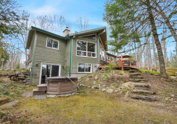 green cottage with walkout basement and hot tub. Stairs leading off the deck. Blue skies.