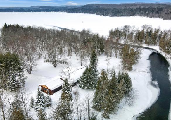House surrounded by trees with a river leading to the lake. Snow on the ground
