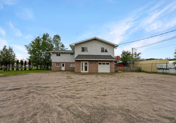 Red brick on bottom level and siding on top level, gravel parking lot and blue sky