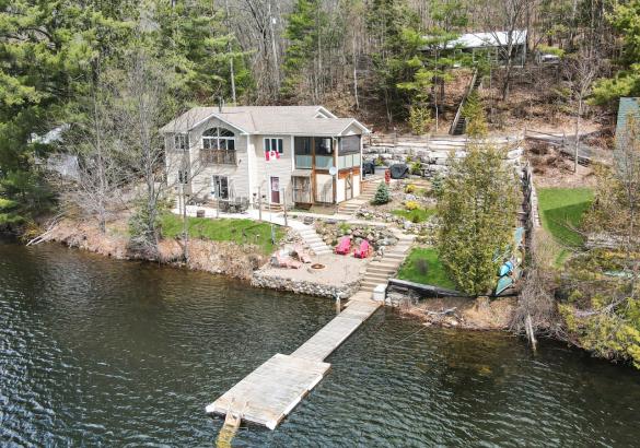 white cottage with landscaping to the lake, dock in the lake, and a cottage up behind