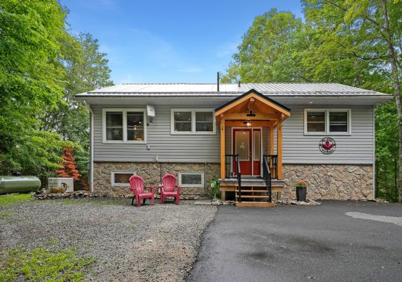 stone and grey home, covered front porch with red door and 2 red muskoka chairs