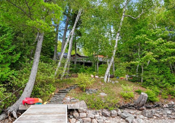 Cottage hidden behind the trees, rocky shoreline, stairs up to firepit area