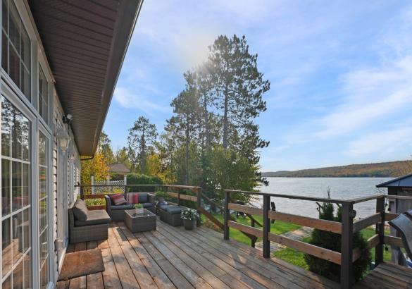 deck with seating area over looking a lake with trees and blue sky